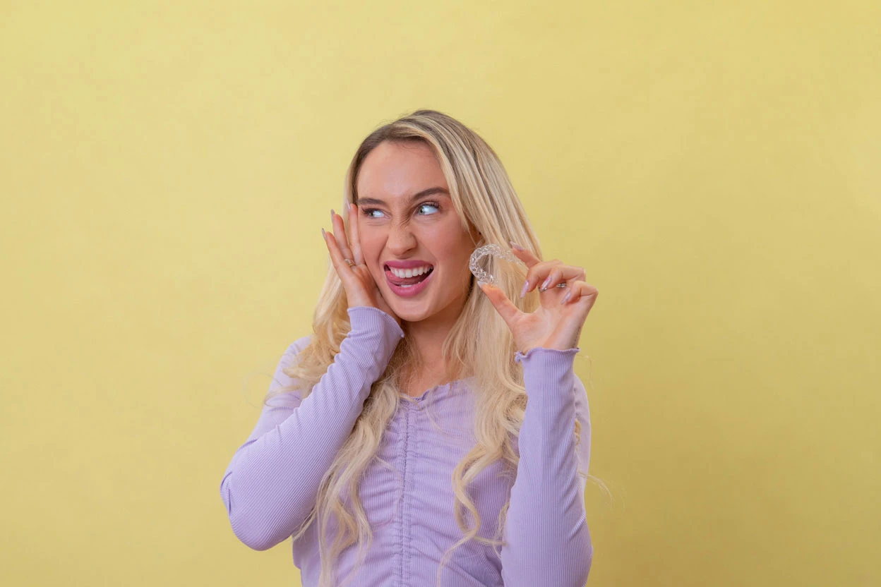 mujer mostrando sus dientes con alineadores invisibles en su mano